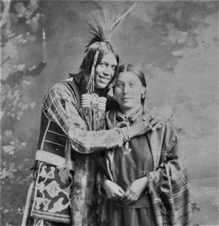 Native American couple in traditional attire embracing, vintage photo revealing real lives from a century ago.