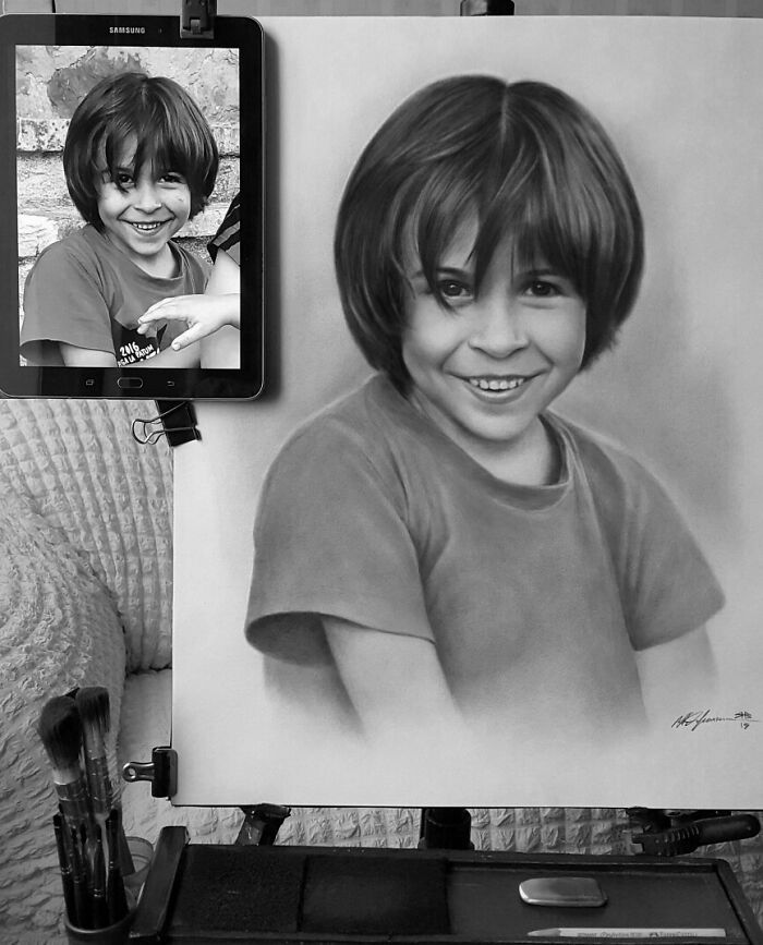 A hyper-realistic pencil portrait of a smiling child, displayed beside a photo reference on a tablet.