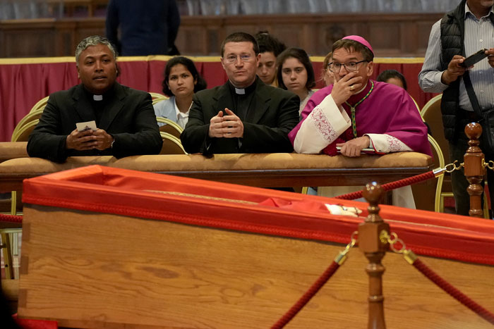 Clergy and attendees beside Pope Francis' open casket in the Vatican, sparking mixed reactions. Clergy and attendees beside Pope Francis' open casket in the Vatican, sparking mixed reactions.