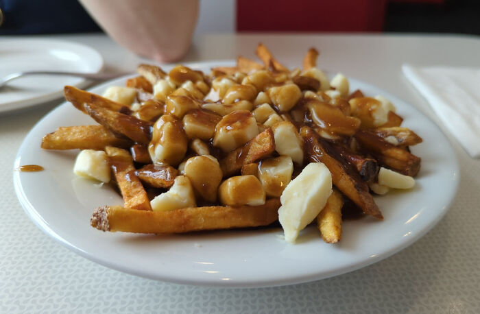 Plate of poutine with fries, cheese curds, and gravy from different countries' top dish menu.
