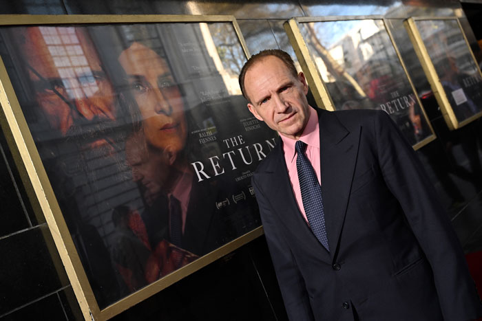 Hollywood icon in a suit poses by film poster at an event, showcasing a polished and formal look. Hollywood icon in a suit poses by film poster at an event, showcasing a polished and formal look.