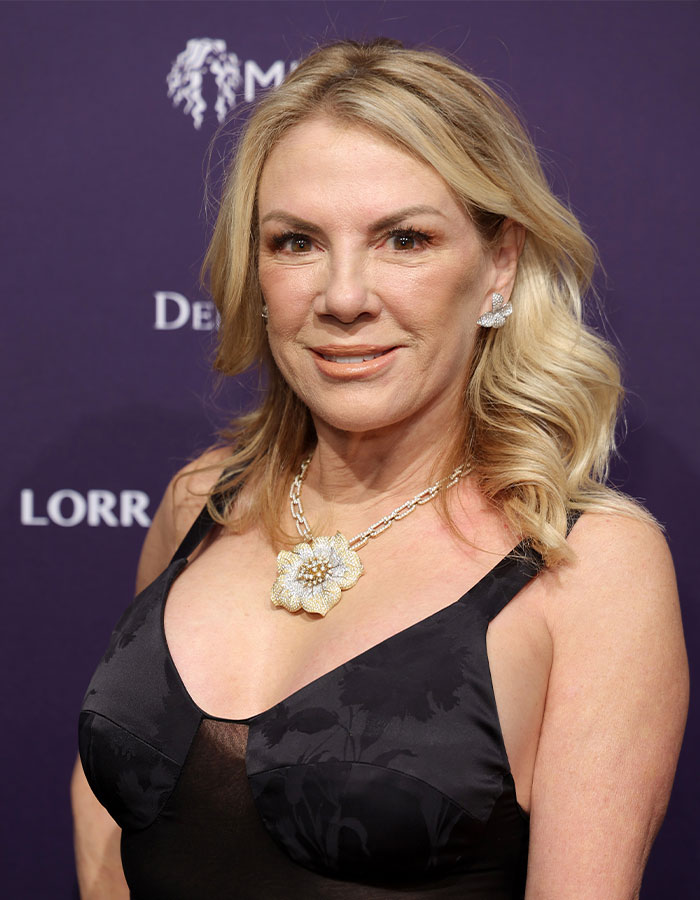 Woman in black dress smiling, with blonde hair and floral necklace, on red carpet. Woman in black dress smiling, with blonde hair and floral necklace, on red carpet.