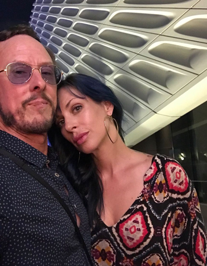 A couple posing in front of a modern architectural background, related to Weezer bassist and lawyer costs discussion. A couple posing in front of a modern architectural background, related to Weezer bassist and lawyer costs discussion.