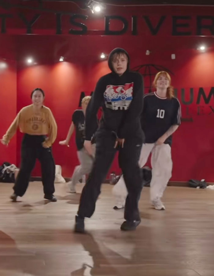 Dancer in a black hoodie and baggy pants leading a group routine, showcasing impressive moves in a studio setting. Dancer in a black hoodie and baggy pants leading a group routine, showcasing impressive moves in a studio setting.