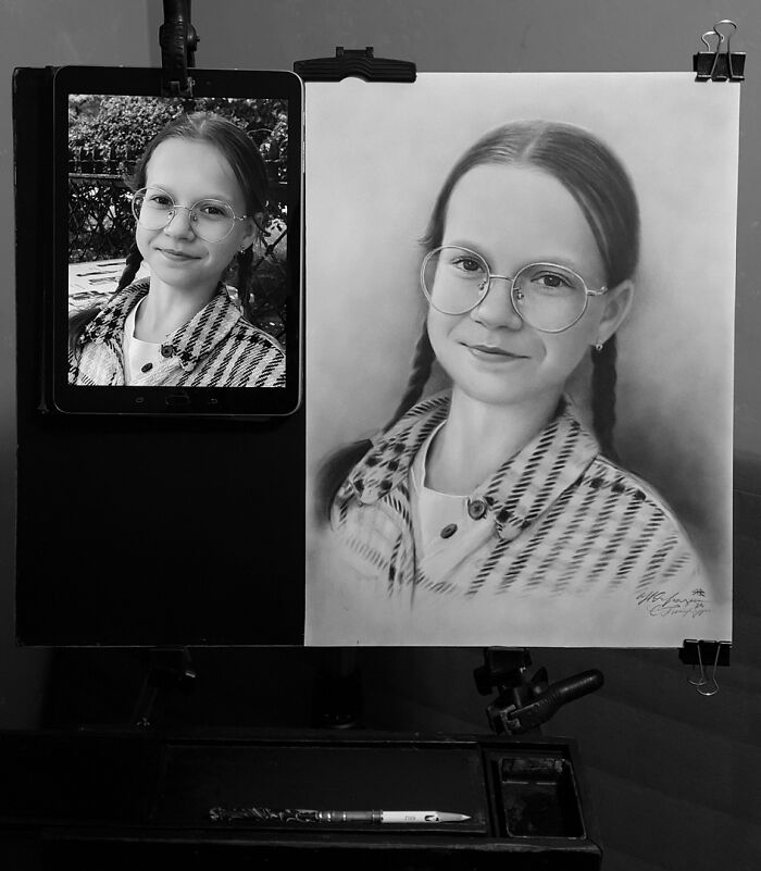 Hyper-realistic pencil portrait of a girl with glasses, next to reference photo on a tablet.