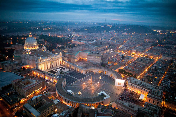 St. Peter's Square at dusk, lights illuminating as thousands gather for Pope Francis's final farewell. St. Peter's Square at dusk, lights illuminating as thousands gather for Pope Francis's final farewell.