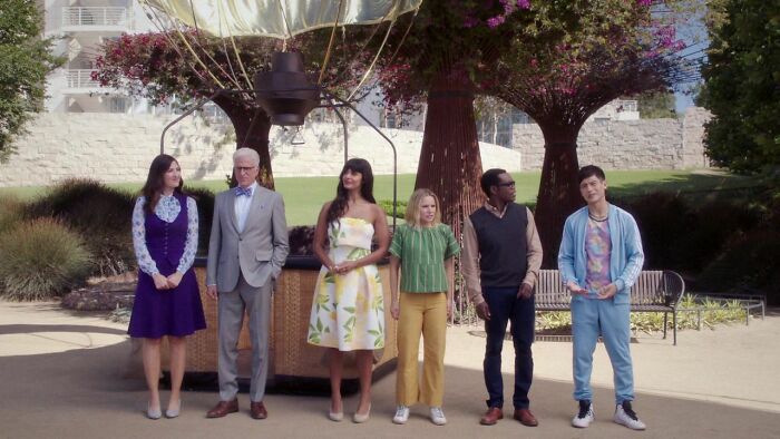 Cast of a popular TV show standing outdoors in a garden setting, under two large, floral trees.