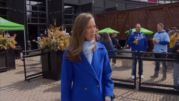 TV reporter in a blue coat appears shocked in a public outdoor setting with people in the background. TV reporter in a blue coat appears shocked in a public outdoor setting with people in the background.