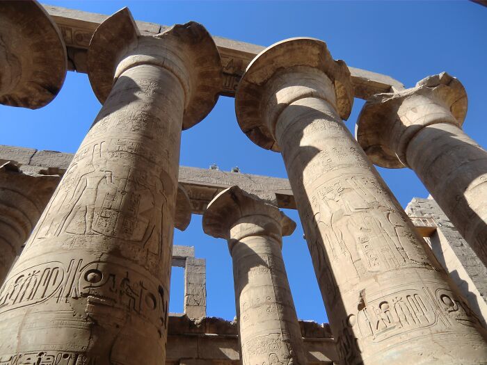 Ancient man-made stone pillars with detailed hieroglyphics under a clear blue sky at a historic archaeological site.