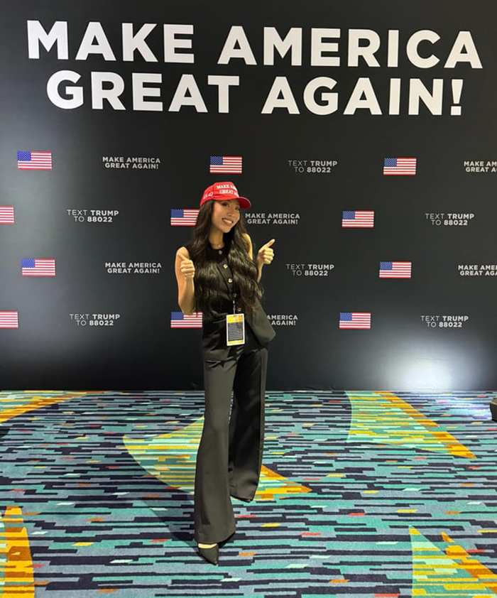 Influencer at a MAGA event, wearing a red cap, standing in front of a "Make America Great Again" sign. Influencer at a MAGA event, wearing a red cap, standing in front of a "Make America Great Again" sign.