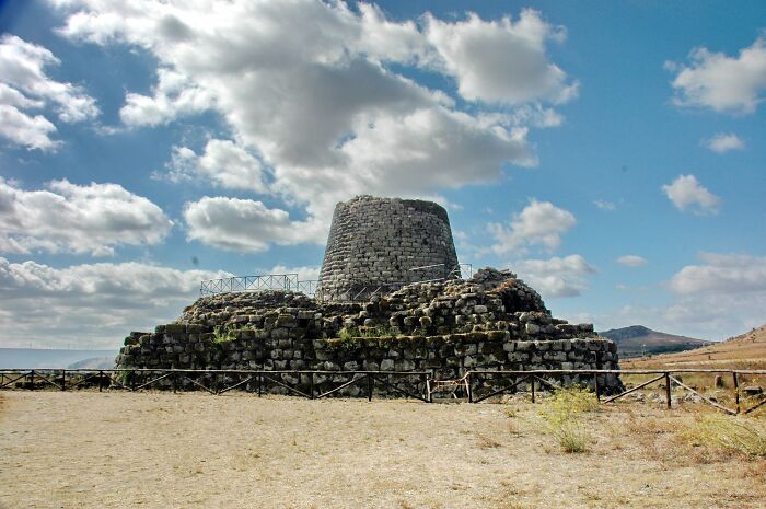 Ancient man-made stone structure on a hill under a cloudy sky, showcasing impressive historical architecture.