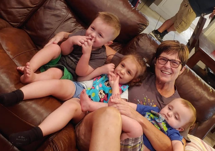 Grandma sitting on a sofa with three toddlers, smiling and holding them on her lap. Grandma sitting on a sofa with three toddlers, smiling and holding them on her lap.