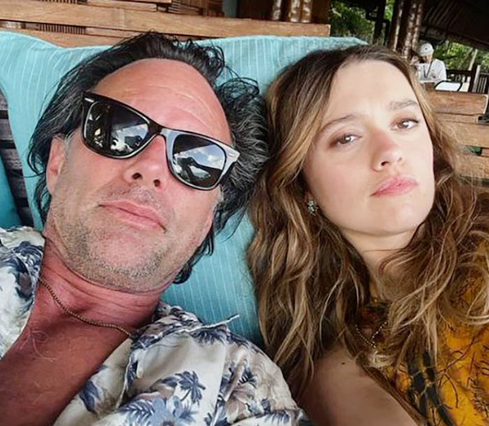 A man in sunglasses and a floral shirt with a woman, both relaxing on a lounge chair outdoors. A man in sunglasses and a floral shirt with a woman, both relaxing on a lounge chair outdoors.