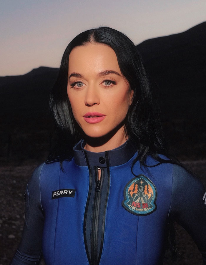 A person wearing a Blue Origin spacesuit at dusk, with mountains in the background. A person wearing a Blue Origin spacesuit at dusk, with mountains in the background.