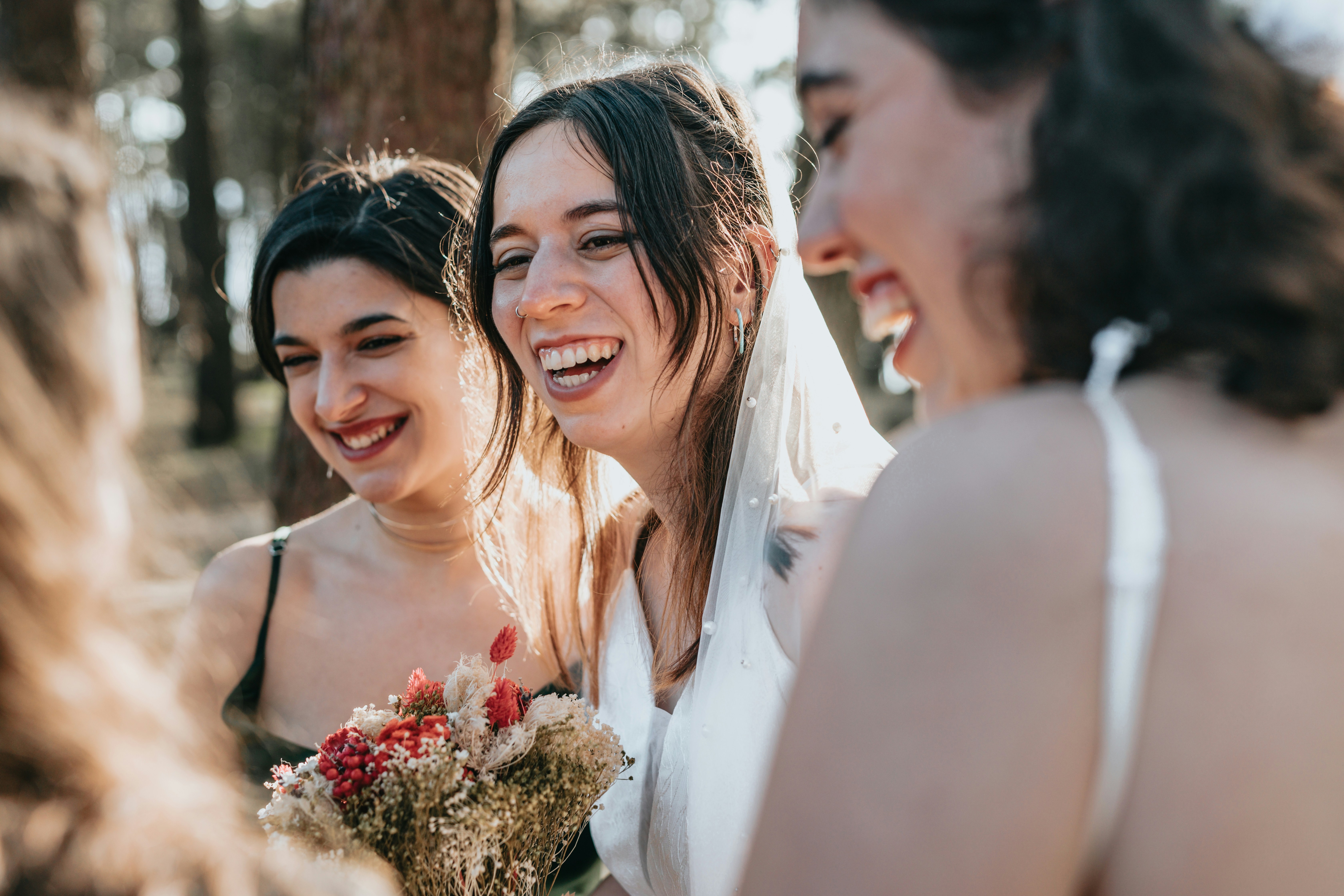 Bride laughing with bridesmaids outdoors, holding a bouquet, highlighting wedding confidence. Bride laughing with bridesmaids outdoors, holding a bouquet, highlighting wedding confidence.