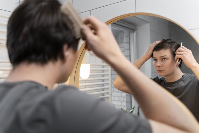 Man combing hair in a bathroom mirror, focused and introspective, representing the concept of a bully reflecting on actions.