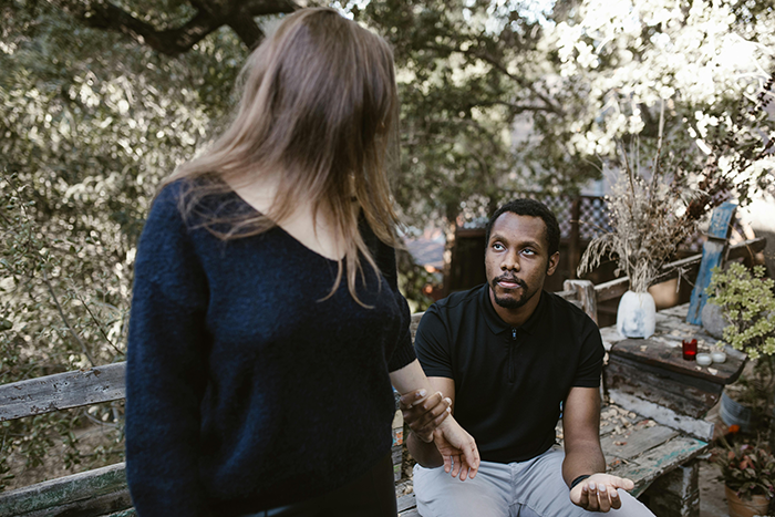 A woman and man having a serious conversation on a rustic outdoor bench, surrounded by greenery and dried plants. A woman and man having a serious conversation on a rustic outdoor bench, surrounded by greenery and dried plants.