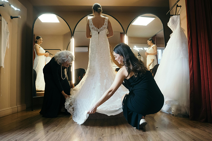 Woman helping bride adjust dress in fitting room, showcasing second mom role. Woman helping bride adjust dress in fitting room, showcasing second mom role.