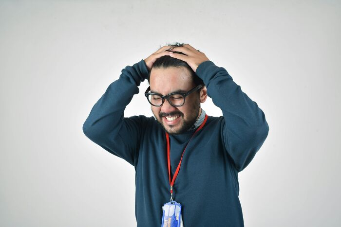 A frustrated man in glasses, wearing a blue sweater, clutching his head in distress.