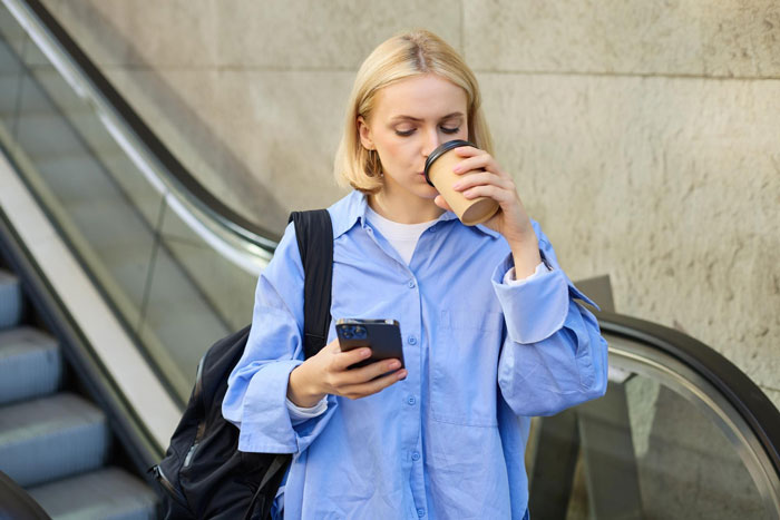 Blonde woman at airport, drinking coffee while using phone. Blonde woman at airport, drinking coffee while using phone.