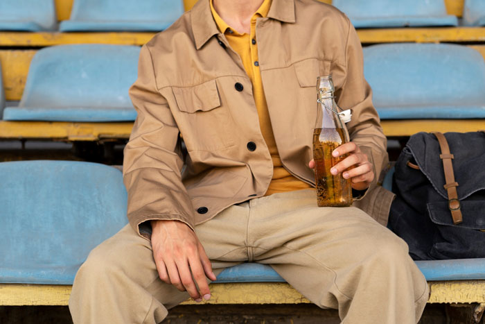 Person seated holding a bottle, representing foods and drinks to avoid at the airport. Person seated holding a bottle, representing foods and drinks to avoid at the airport.
