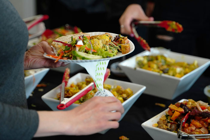 Person holding a plate of assorted foods at a buffet, highlighting choices to avoid consuming at the airport. Person holding a plate of assorted foods at a buffet, highlighting choices to avoid consuming at the airport.