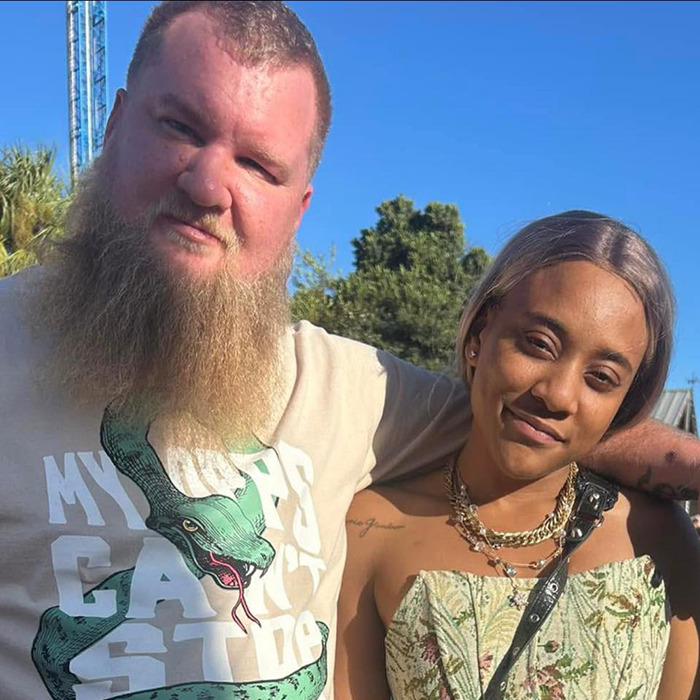 A man and woman standing together outdoors, with trees in the background, in a casual setting. A man and woman standing together outdoors, with trees in the background, in a casual setting.