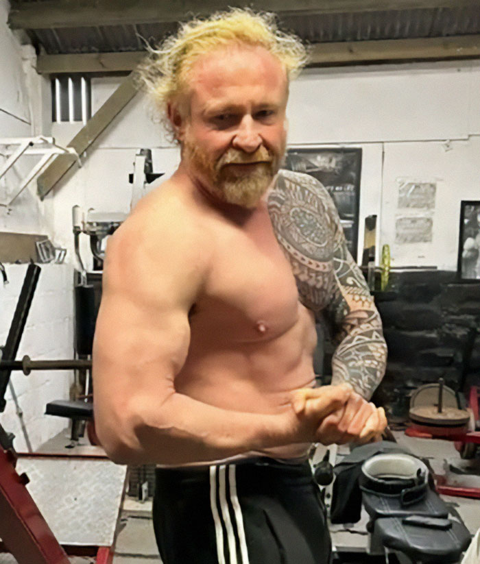 Man flexing muscles in a gym, wearing black pants, representing family tragedy keywords. Man flexing muscles in a gym, wearing black pants, representing family tragedy keywords.
