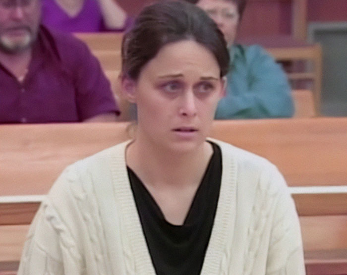 Woman sitting in court with a worried expression, wearing a white sweater. Woman sitting in court with a worried expression, wearing a white sweater.