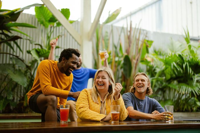 Group of tourists laughing at an outdoor venue, enjoying drinks, with plants in the background.