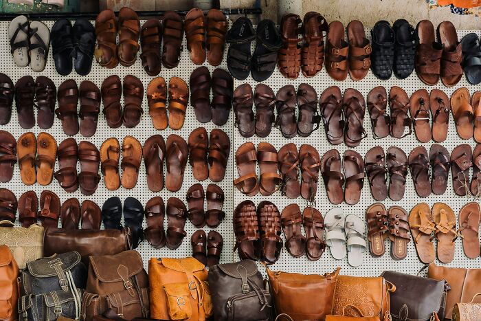 Various leather sandals and bags displayed at a market, depicting tourist shopping habits.