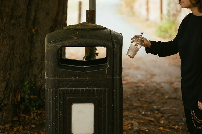 Person throwing a plastic cup in a public trash bin, illustrating an American tourist's environmental habit.