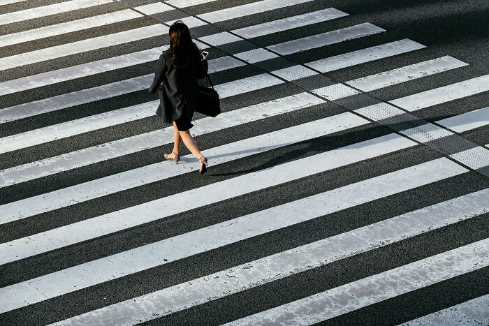 Woman in black coat walking on a zebra crossing from an elevated view.