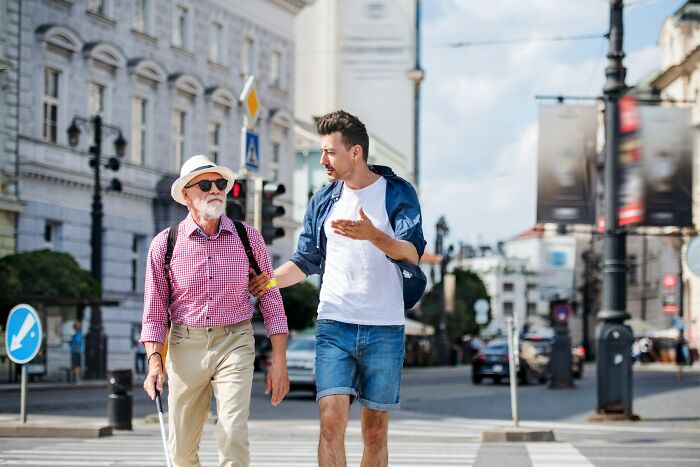 Two men walking on a city street, one in a hat and sunglasses, showcasing American tourist fashion and style.