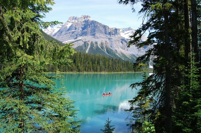 Canoe on a serene lake framed by trees with mountains in the background, hinting at American tourist sightings.