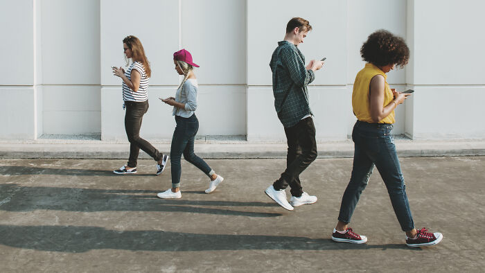 Four people walking and using phones, showcasing common American tourist behavior.