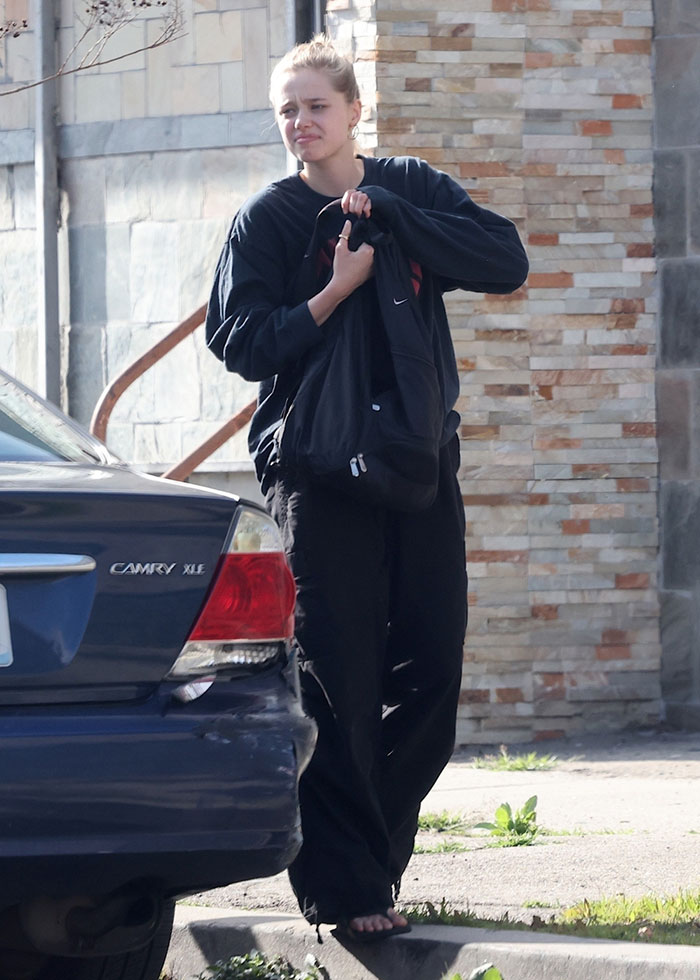Young person in casual clothing holding a bag, standing next to a parked car on a sunny day. Young person in casual clothing holding a bag, standing next to a parked car on a sunny day.