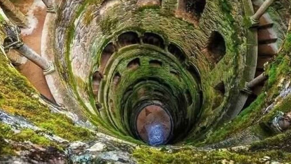 Stone spiral staircase covered in moss inside an ancient archaeological architecture site viewed from above.