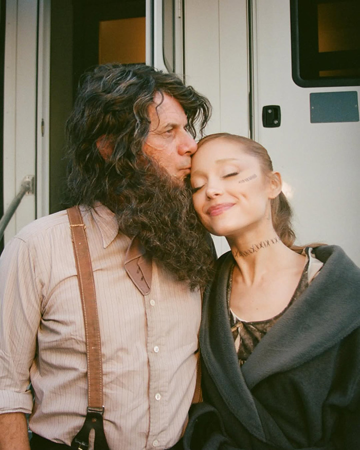Ariana Grande showcases tattoos and new hair, smiling with a man in costume outside. Ariana Grande showcases tattoos and new hair, smiling with a man in costume outside.