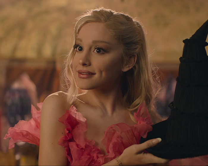 Ariana Grande shows off tattoos and new hair while holding a black hat, wearing a pink ruffled dress. Ariana Grande shows off tattoos and new hair while holding a black hat, wearing a pink ruffled dress.