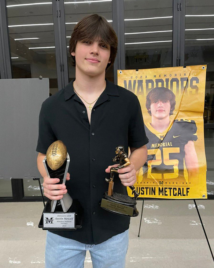 Young man standing with two trophies, wearing a black shirt, Austin Metcalf banner in the background. Young man standing with two trophies, wearing a black shirt, Austin Metcalf banner in the background.