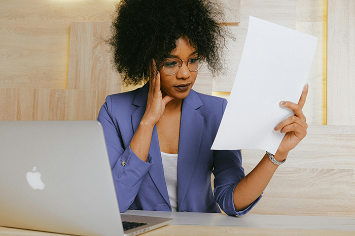 Woman in purple blazer reading a document at a desk with a laptop, contemplating issues about marriage and name decisions. Woman in purple blazer reading a document at a desk with a laptop, contemplating issues about marriage and name decisions.