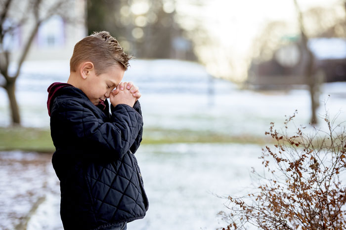 Young boy in a black jacket praying outdoors on a snowy day, reflecting grief and contemplation. Young boy in a black jacket praying outdoors on a snowy day, reflecting grief and contemplation.