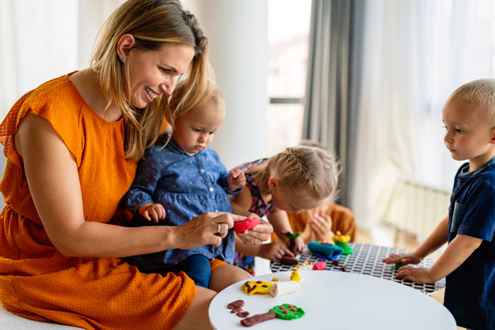 Woman babysitting newborn and children indoors, engaging them with toys and play activities at a table. Woman babysitting newborn and children indoors, engaging them with toys and play activities at a table.