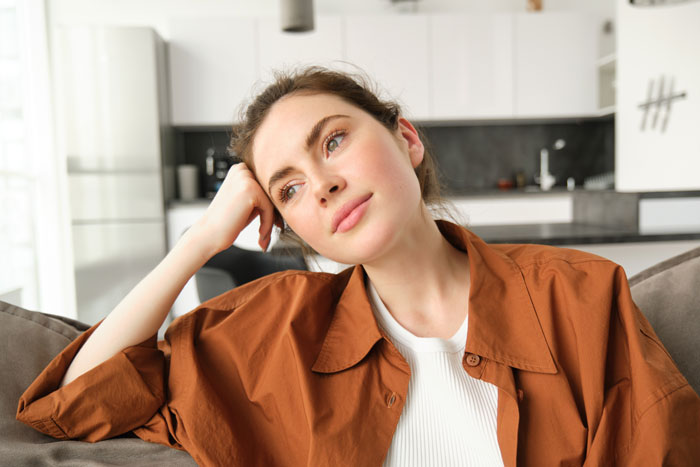 Young woman with a thoughtful expression sitting on a couch, reflecting on babysitting and payment fairness issues. Young woman with a thoughtful expression sitting on a couch, reflecting on babysitting and payment fairness issues.