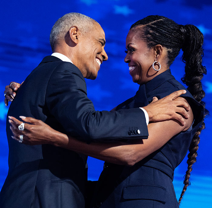 Former president, smiling, embraces his wife on stage during a public appearance. Former president, smiling, embraces his wife on stage during a public appearance.