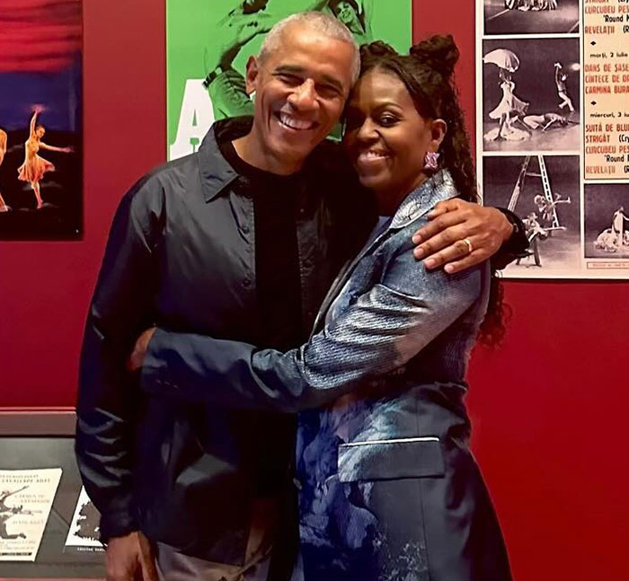 Michelle Obama smiling with spouse, embracing in front of colorful posters, addressing divorce rumors. Michelle Obama smiling with spouse, embracing in front of colorful posters, addressing divorce rumors.