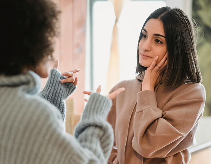 Two women engaged in a serious conversation, one touching her face thoughtfully. Two women engaged in a serious conversation, one touching her face thoughtfully.