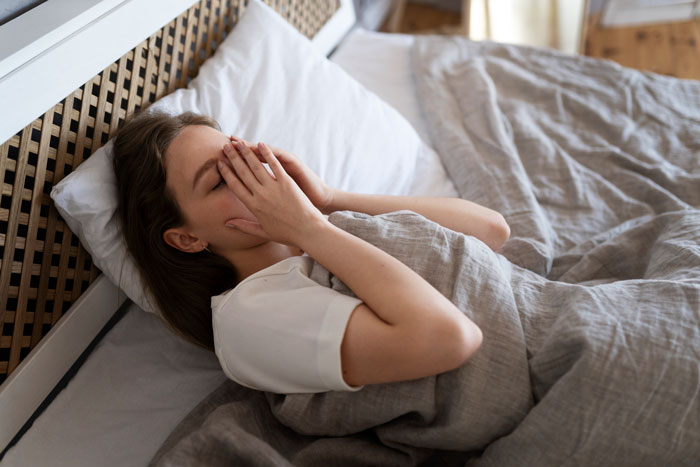 Woman covering face with hands in bed, showing tiredness and lack of proper sleep after weeks of poor rest.