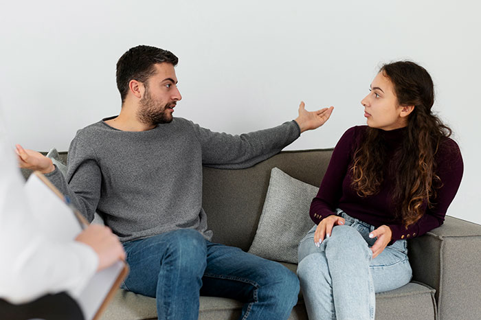 Couple in a heated discussion on the sofa, man gestures widely while woman looks concerned. Couple in a heated discussion on the sofa, man gestures widely while woman looks concerned.